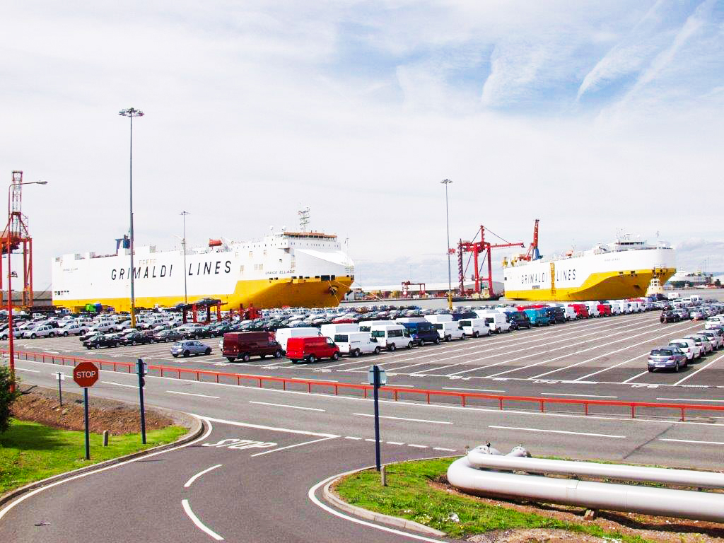 Cars being off-loaded by a boat at a port.